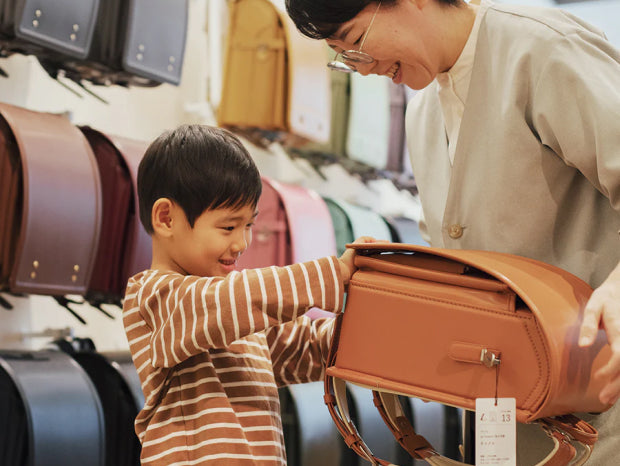 キャメルのランドセルを開けようとする子どもとそれを手伝う店員